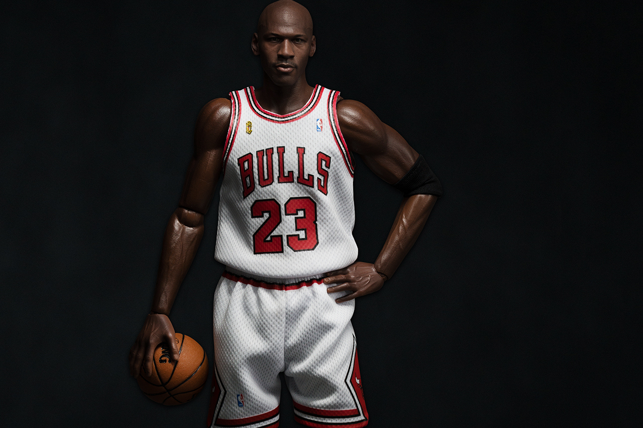 A imagem mostra o jogador de basquete Michael Jordan, em um fundo preto, com uma camise do time de basquete bulls e com uma bola em suas mãos