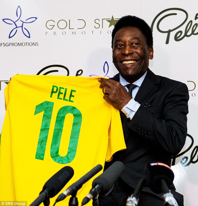 A imagem mpstra o jogador mde futebol Pelé, segurando uma camisa do time de futebol brasileiro enquanto sorri para as cameras