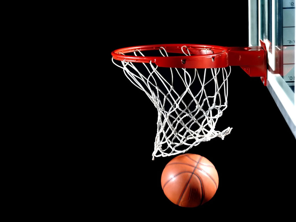 A imagem mostra uma bola de basquete, com uma quadra vazia e uma cesta de basquete ao fundo, em um ambiente escuro, onde se da destaque, por meio de luzes, a bola e a tabela/aro da cesta